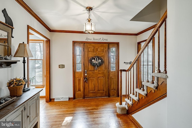 entrance foyer with visible vents, baseboards, stairs, ornamental molding, and light wood finished floors