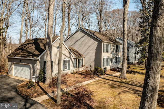 view of side of property with a garage, a shingled roof, and aphalt driveway