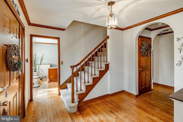 foyer with arched walkways, baseboards, stairway, light wood-type flooring, and crown molding