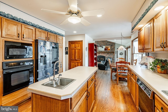 kitchen featuring lofted ceiling, light wood-style flooring, black appliances, a fireplace, and a sink