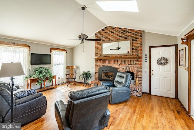 living area featuring ceiling fan, vaulted ceiling with skylight, a fireplace, and wood finished floors