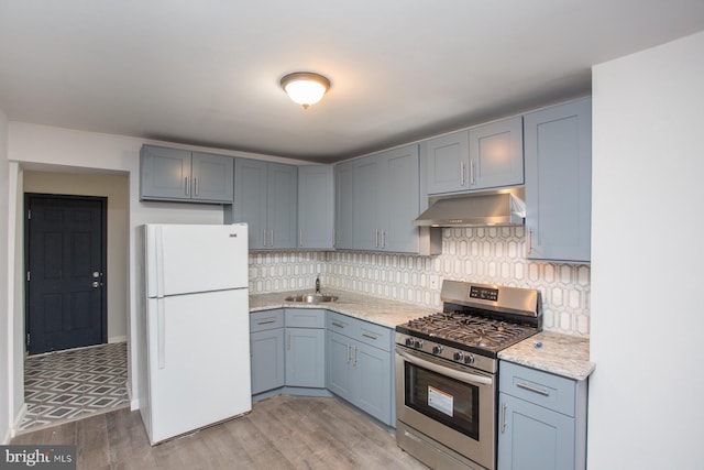 kitchen with light wood-style floors, freestanding refrigerator, under cabinet range hood, stainless steel range with gas cooktop, and a sink