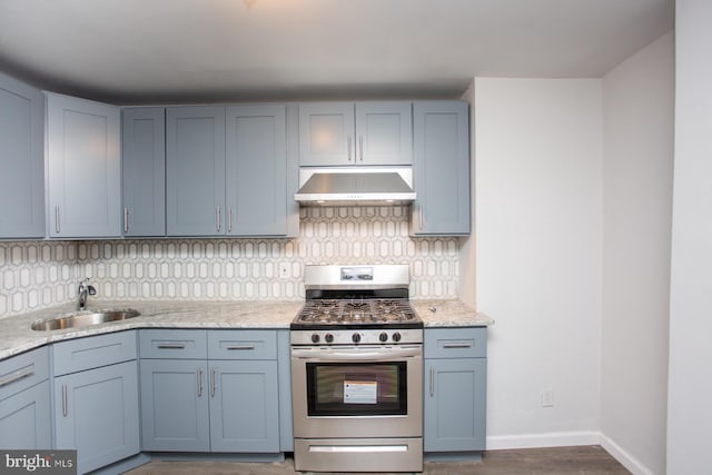 kitchen with tasteful backsplash, baseboards, gas range, under cabinet range hood, and a sink