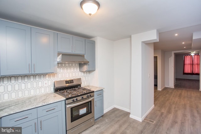 kitchen with under cabinet range hood, tasteful backsplash, baseboards, and gas range