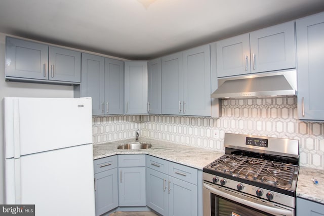 kitchen with tasteful backsplash, freestanding refrigerator, under cabinet range hood, a sink, and gas stove