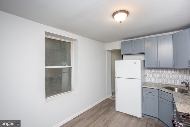 kitchen featuring wood finished floors, black gas stove, a sink, baseboards, and freestanding refrigerator