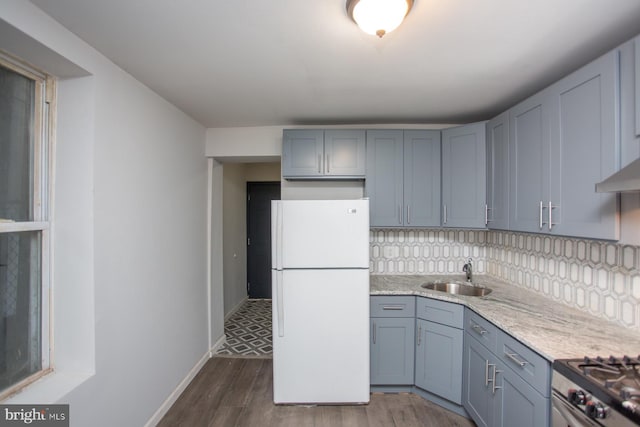 kitchen featuring dark wood-style flooring, decorative backsplash, freestanding refrigerator, a sink, and baseboards