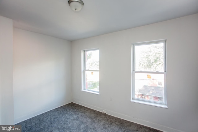 empty room featuring dark colored carpet and baseboards