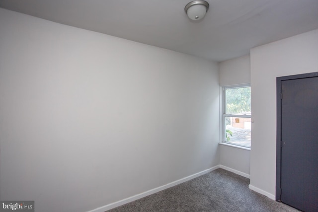 unfurnished room with baseboards and dark carpet