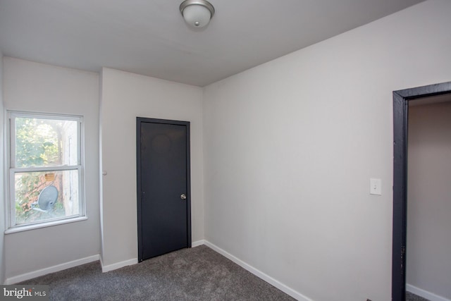 unfurnished room with baseboards and dark colored carpet