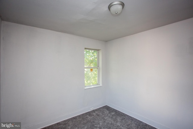 spare room with dark colored carpet and baseboards