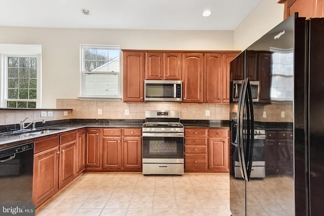 kitchen with brown cabinetry, a sink, black appliances, backsplash, and light tile patterned flooring