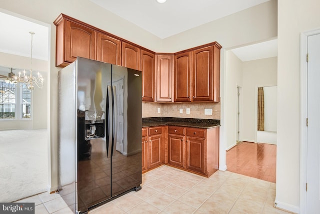 kitchen featuring light tile patterned flooring, black fridge, decorative backsplash, brown cabinetry, and an inviting chandelier