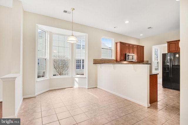 kitchen with visible vents, dark countertops, a breakfast bar area, stainless steel microwave, and black fridge