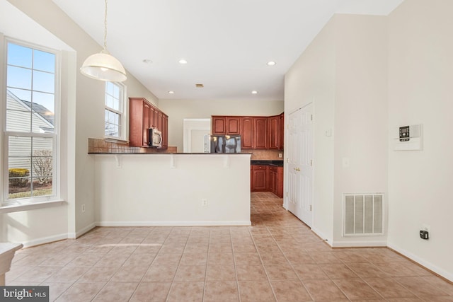 kitchen with visible vents, dark countertops, stainless steel microwave, a peninsula, and fridge