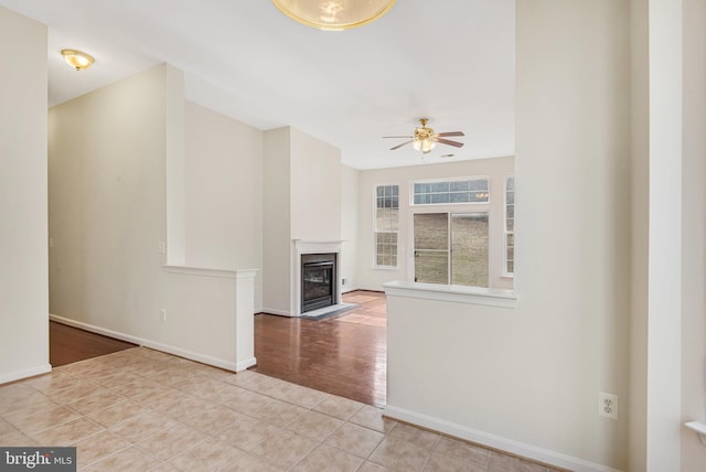 unfurnished living room with a fireplace with flush hearth, baseboards, ceiling fan, and tile patterned flooring