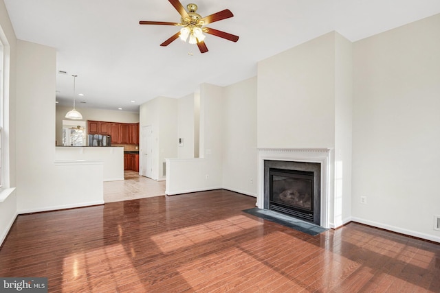 unfurnished living room with a fireplace with flush hearth, ceiling fan, wood finished floors, and baseboards