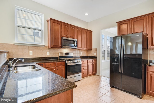 kitchen featuring plenty of natural light, decorative backsplash, appliances with stainless steel finishes, dark stone countertops, and a sink