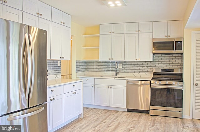 kitchen featuring white cabinets, appliances with stainless steel finishes, light wood-type flooring, open shelves, and a sink