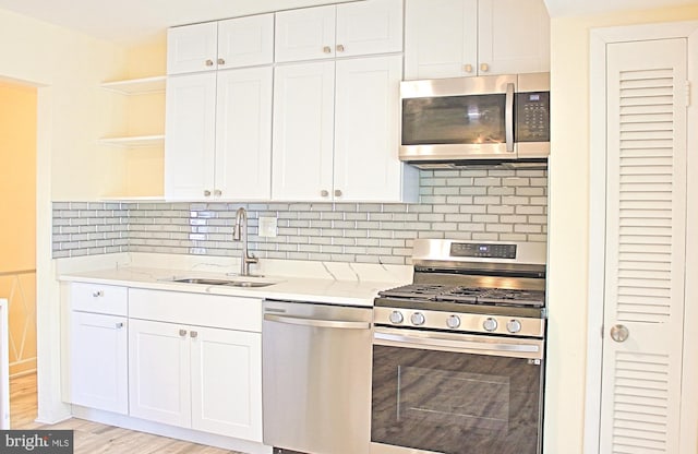 kitchen with white cabinets, stainless steel appliances, open shelves, and a sink