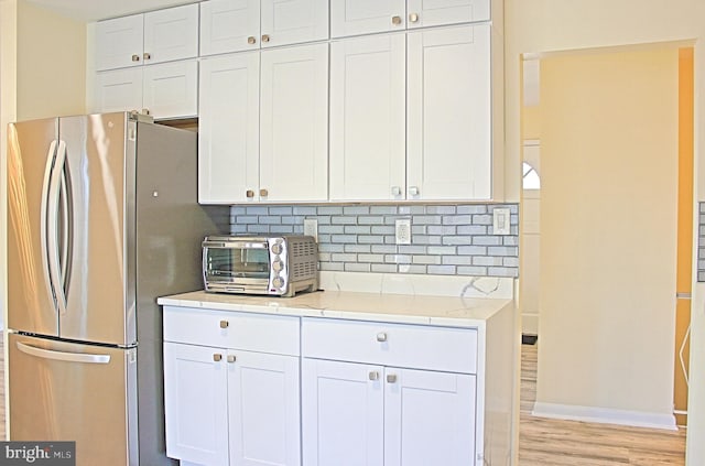 kitchen featuring light wood-style floors, tasteful backsplash, white cabinetry, and freestanding refrigerator