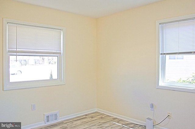 empty room with light wood-style floors, visible vents, and baseboards