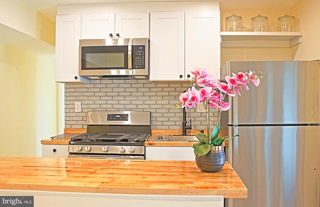 kitchen with stainless steel appliances, butcher block counters, a sink, white cabinetry, and tasteful backsplash