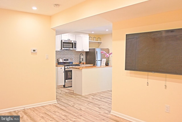 kitchen featuring light wood finished floors, stainless steel appliances, backsplash, white cabinetry, and a sink