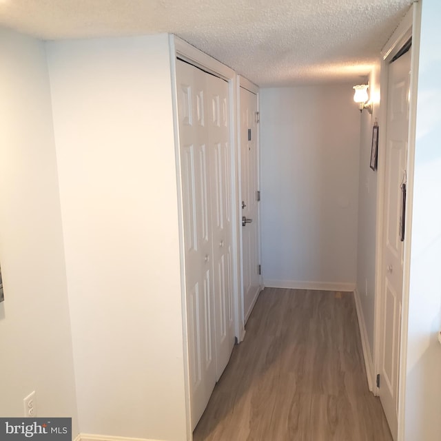 corridor with a textured ceiling, light wood finished floors, and baseboards