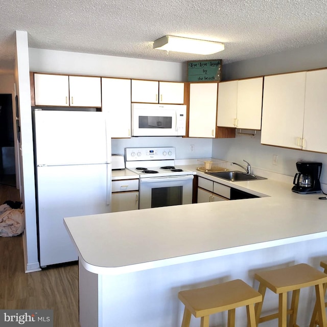 kitchen with a peninsula, white appliances, wood finished floors, a sink, and light countertops