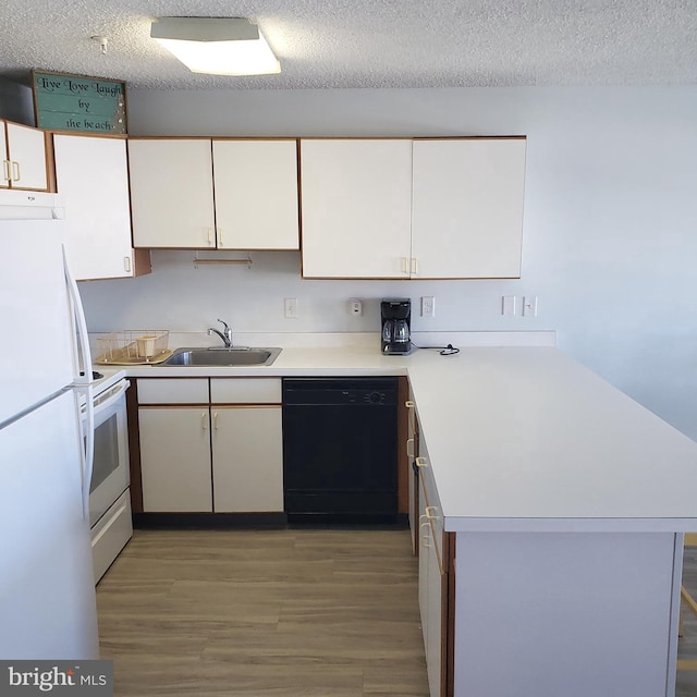 kitchen featuring a peninsula, white appliances, a sink, white cabinets, and light countertops