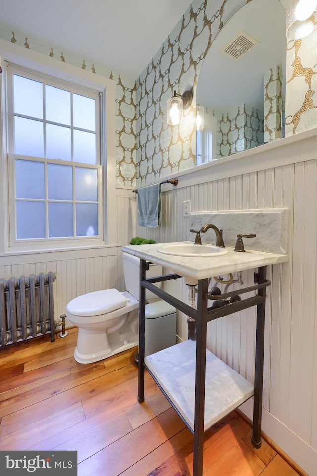 half bathroom featuring hardwood / wood-style floors, radiator, visible vents, wallpapered walls, and wainscoting