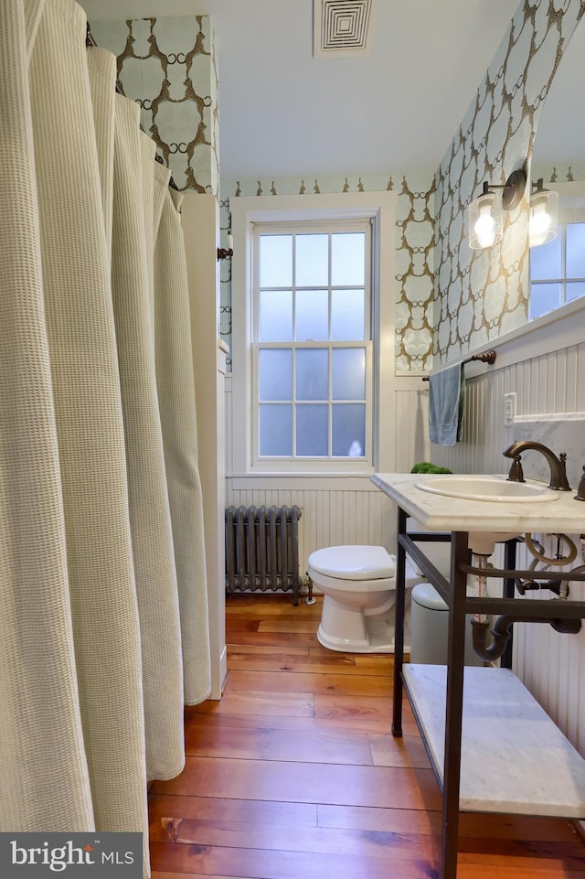 full bathroom featuring visible vents, toilet, hardwood / wood-style flooring, radiator, and wainscoting