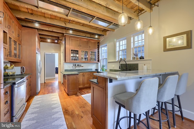 kitchen with a breakfast bar, beamed ceiling, brown cabinetry, and appliances with stainless steel finishes