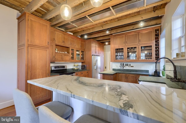 kitchen featuring light stone countertops, a sink, appliances with stainless steel finishes, beamed ceiling, and brown cabinets