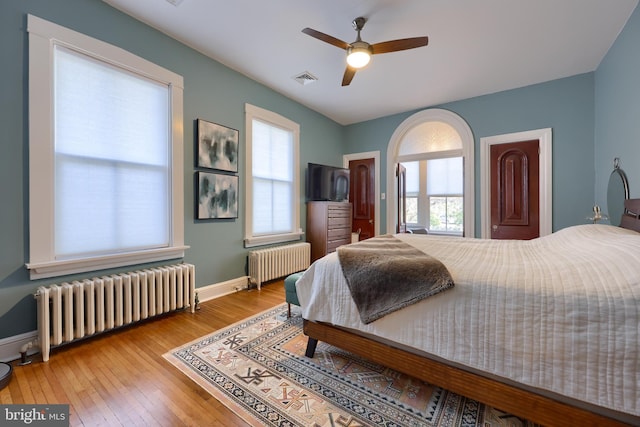 bedroom with multiple windows, hardwood / wood-style floors, and radiator heating unit