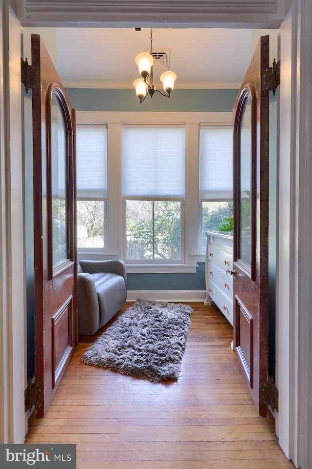 living area with visible vents, light wood-style floors, ornamental molding, and a chandelier