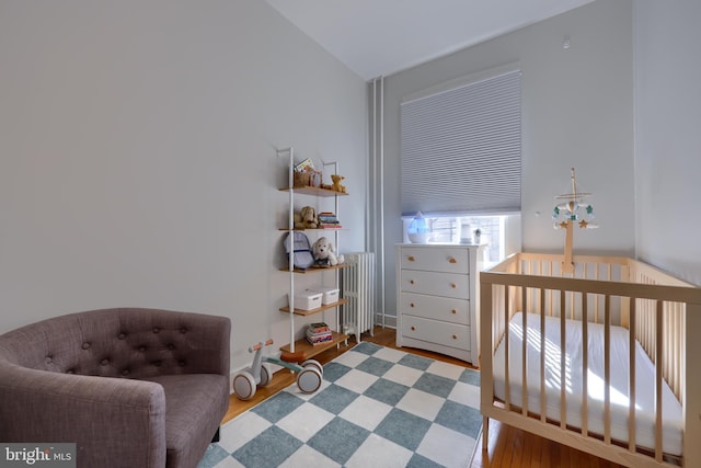 bedroom featuring a crib, vaulted ceiling, radiator, and wood finished floors