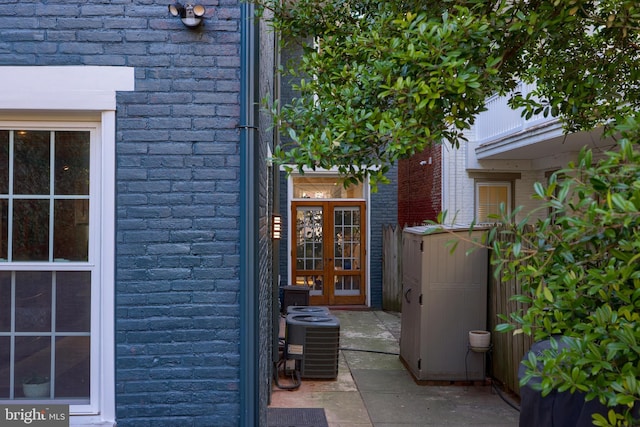 doorway to property featuring brick siding, cooling unit, and french doors