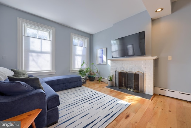 living area with a baseboard heating unit, wood finished floors, and a fireplace