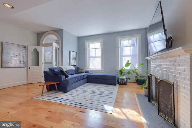 living room featuring a brick fireplace, baseboards, and light wood-type flooring