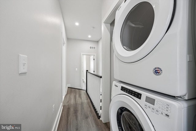 clothes washing area with laundry area, baseboards, visible vents, stacked washer and clothes dryer, and wood finished floors