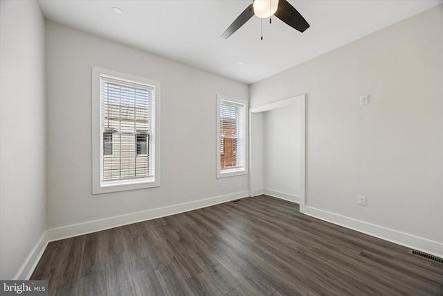 spare room featuring a ceiling fan, visible vents, baseboards, and dark wood-style flooring