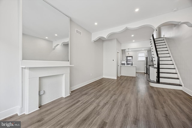 unfurnished living room featuring recessed lighting, wood finished floors, visible vents, baseboards, and stairway