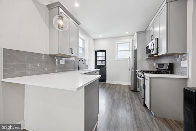 kitchen with appliances with stainless steel finishes, dark wood-style flooring, a peninsula, light countertops, and a sink