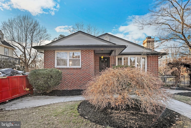 bungalow-style house featuring brick siding, fence, and a chimney