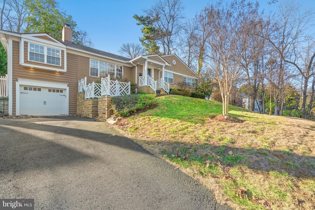 view of front of property with an attached garage, a chimney, aphalt driveway, and a front yard