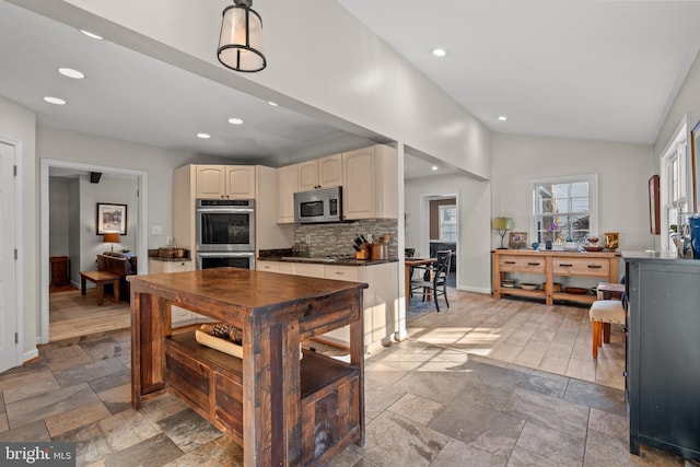 kitchen with cream cabinetry, stainless steel appliances, dark countertops, stone tile flooring, and tasteful backsplash