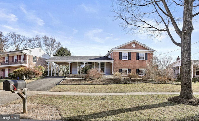 view of front of property with driveway, covered porch, a front yard, an attached carport, and brick siding