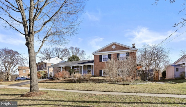 view of front of home featuring fence, a shed, a front lawn, an outdoor structure, and brick siding